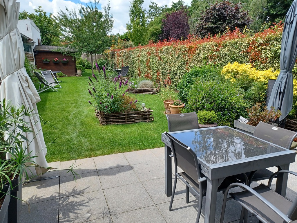 terrasse donnant sur jardin avec table, chaise et parasol.